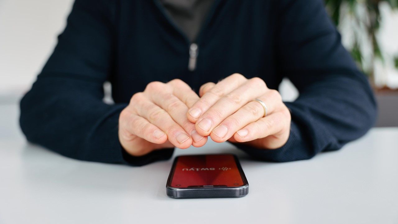 Person hält schützend beide Hände über ein auf dem Tisch liegenden Handy